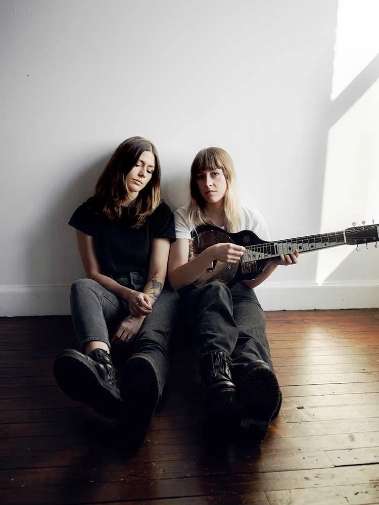 Larkin Poe seated on floor holding a lap steel guitar