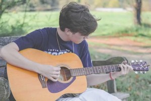 a boy sits on a bench playing his guitar in a park