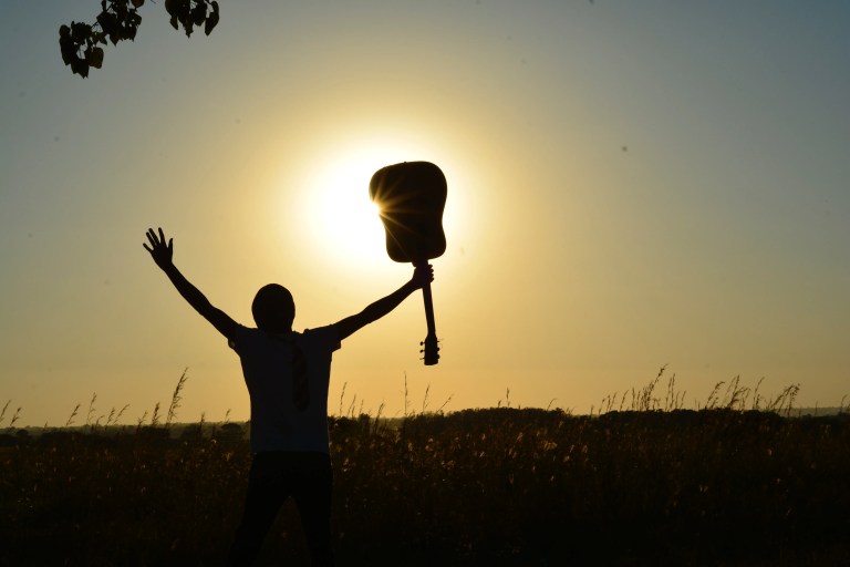 Steve Baughman with arms raised and a guitar in one hand at sunset
