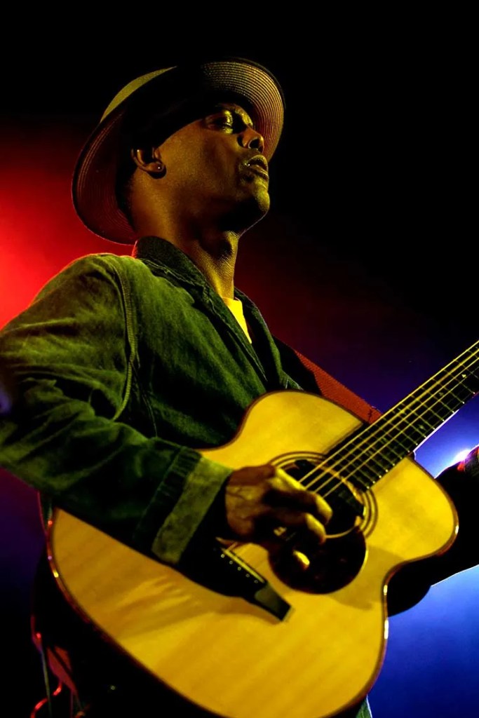 Eric Bibb, eyes closed, picks an acoustic guitar