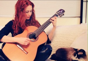 Gretchen Menn with her guitar seated on a white couch